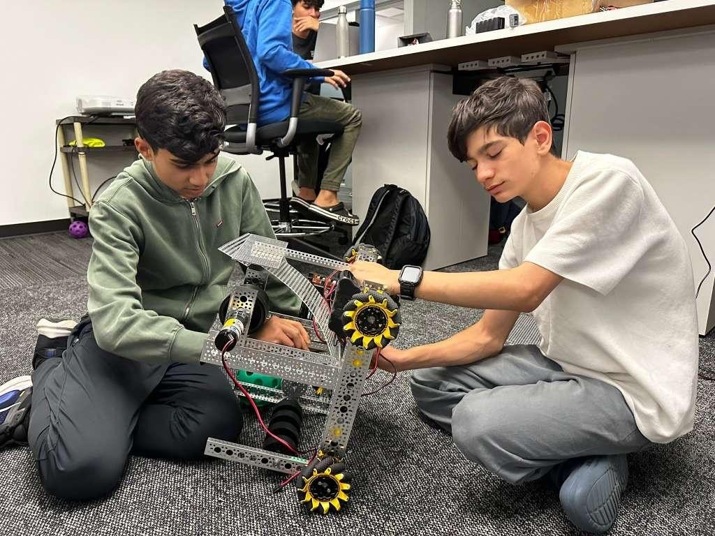 Two students kneeling to work on a robot chassis